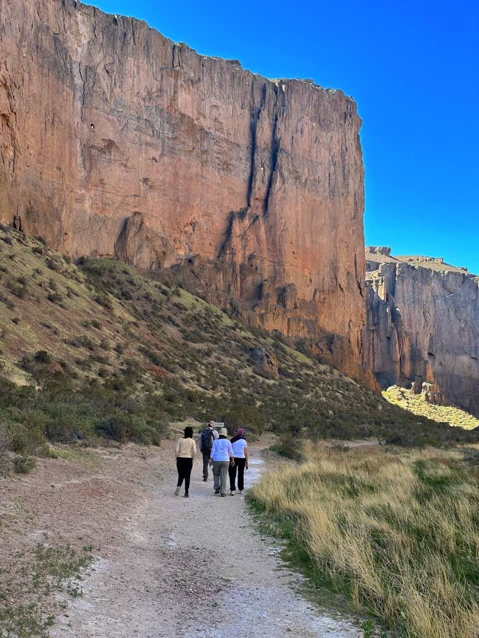 Grupo caminando al pie de la imponente pared de roca de Piedra Parada, Chubut