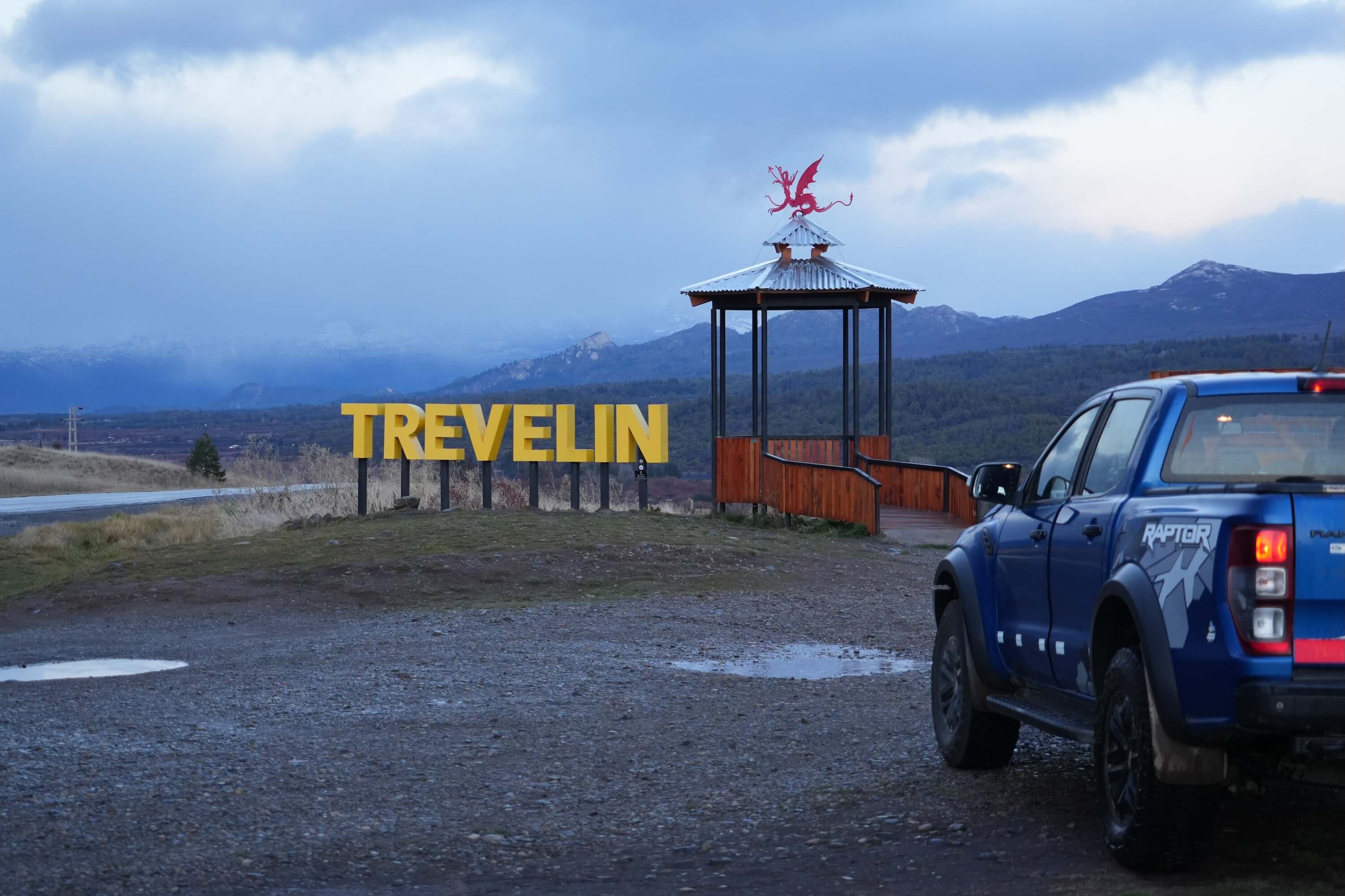 Cartel de Trevelin con el dragón galés y una camioneta 4x4 en el mirador